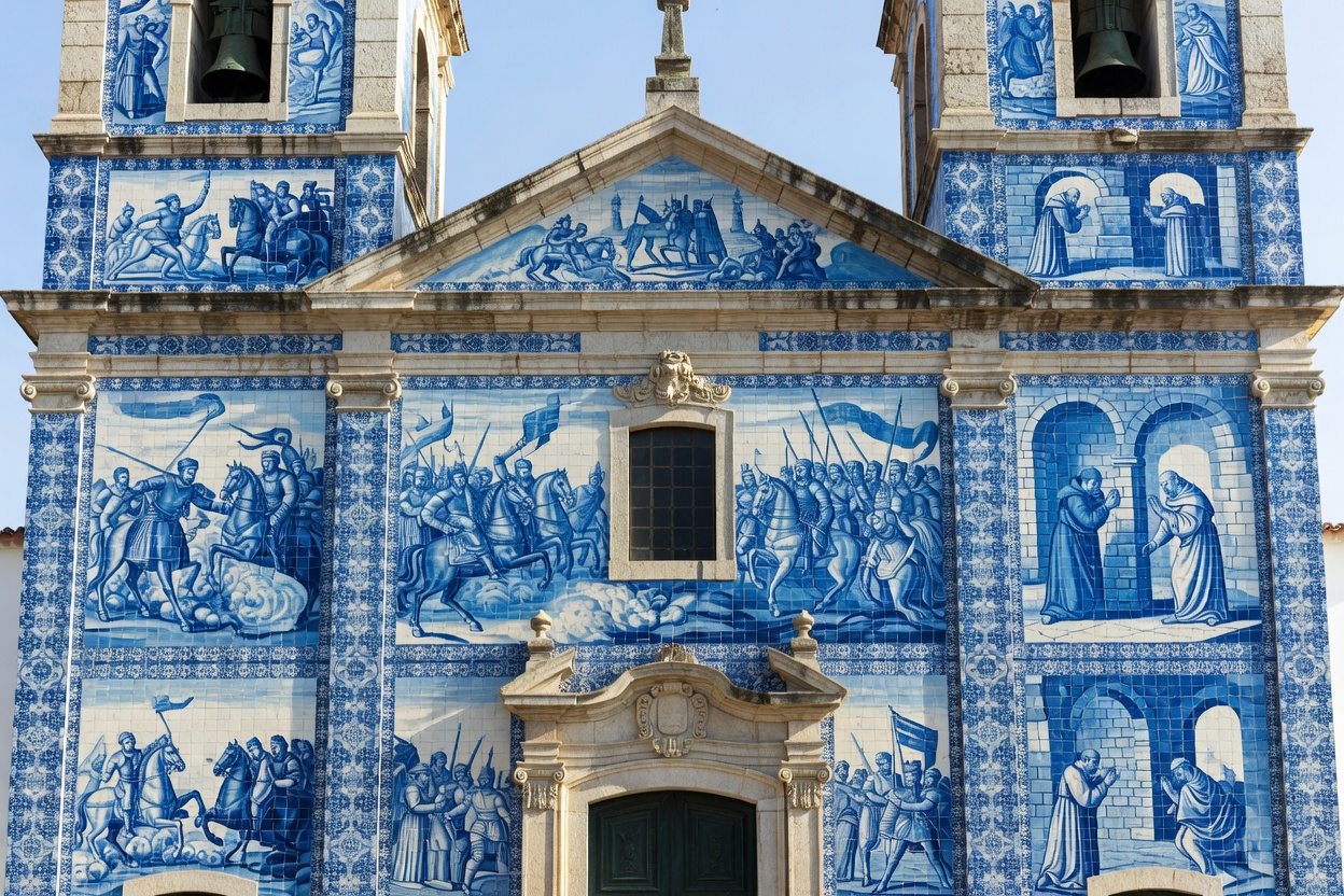 En kirkefasade i Portugal dekket av blå og hvite malte azulejo-fliser som skildrer historiske scener